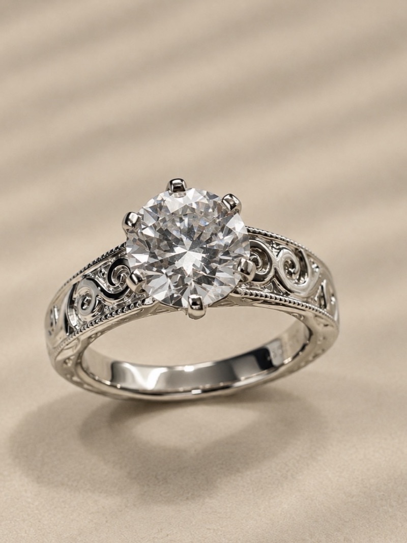 Bague solitaire en or gris sertie d'un diamant rond brillant, épaules gravées de volutes filigranées